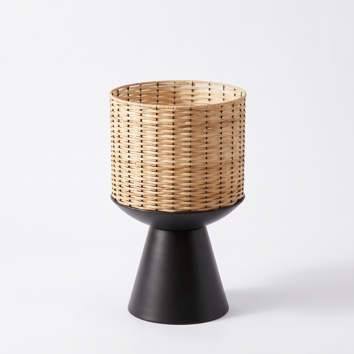 Cache-pot cylindrique en rotin sur socle noir sur fond blanc