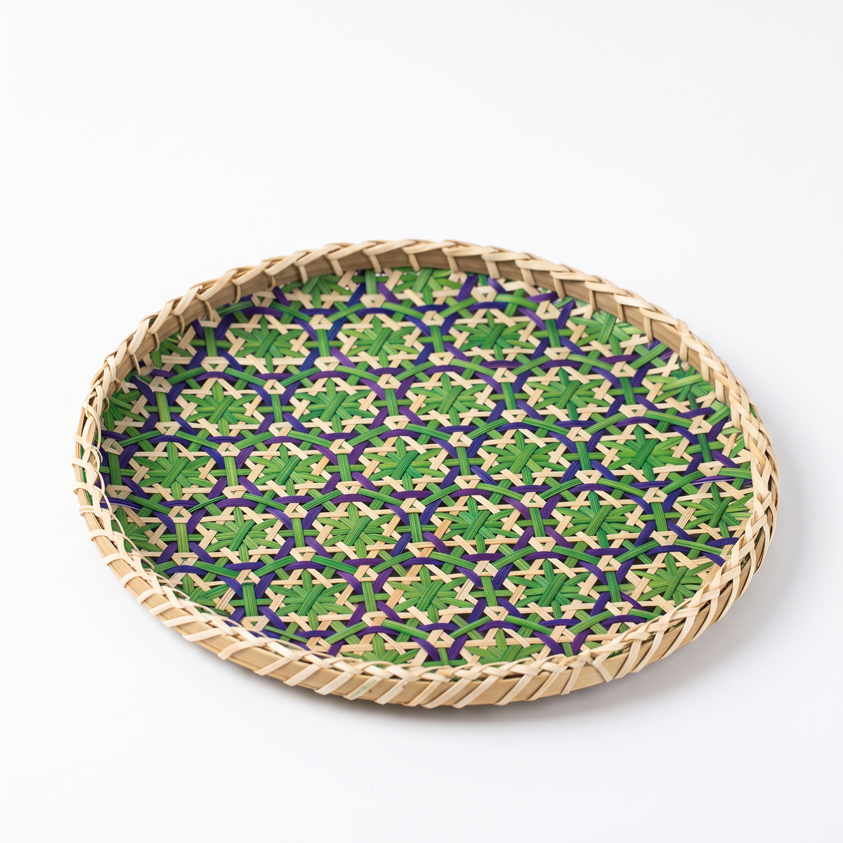 Plateau rond en rotin et bambou à motifs géométriques sur fond blanc
